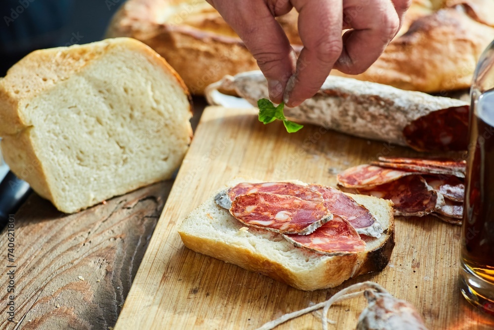 A man's hand throws greens on slices of cured sausage on a piece of white bread. Making a sandwich. The process of making food A man's hand throws greens on slices of cured sausage on a piece of white bread. Making a sandwich. The process of making food
