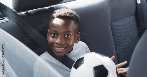 African American boy smiles in the backseat of a car, holding a soccer ball photo