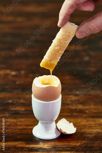 Hand Dipping a Soldier Toast Into a Soft-Boiled Egg in a White Eggcup