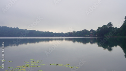 Tranquil view background of the lake with cloudy gray sky and calm water reflection with green water aquatic plant. Natural backgrounds.