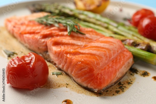 Tasty grilled salmon with tomatoes, asparagus and spices on plate, closeup