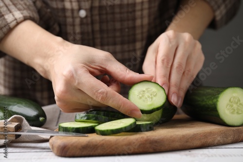Woman putting slice of fresh cucumber onto cutting board, closeup