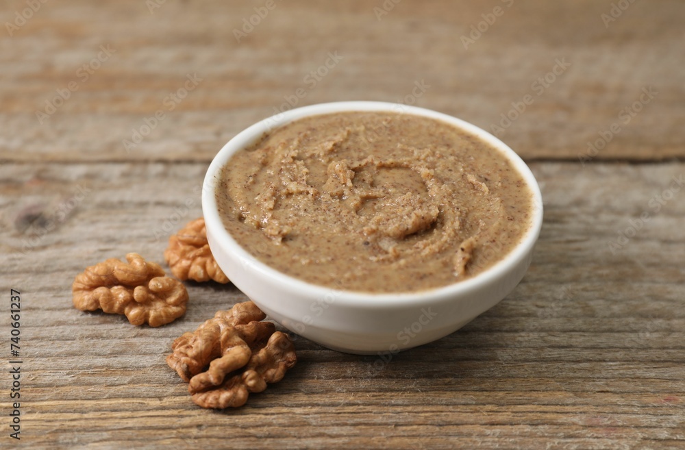 Delicious nut butter in bowl and walnuts on wooden table, closeup Delicious nut butter in bowl and walnuts on wooden table, closeup