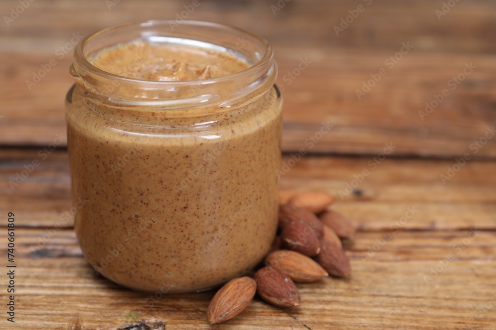 Tasty nut paste in jar and almonds on wooden table, closeup. Space for text Tasty nut paste in jar and almonds on wooden table, closeup. Space for text