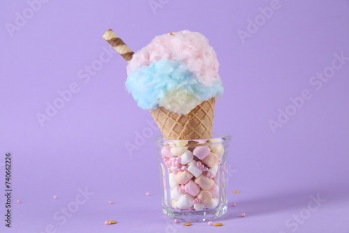 Sweet cotton candy in waffle cone on purple background, closeup
