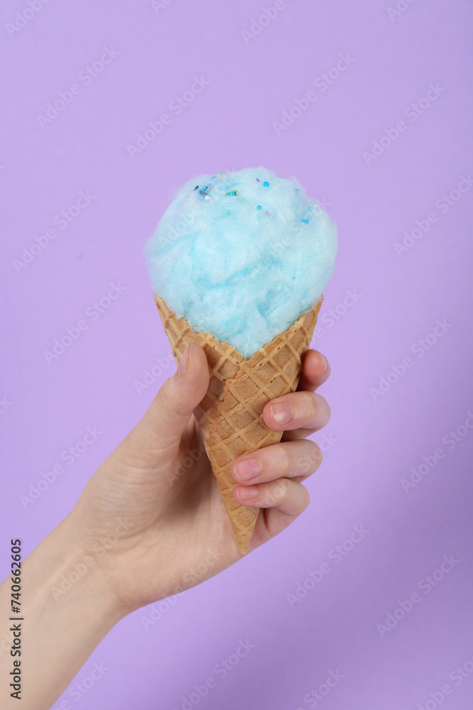 Woman holding waffle cone with cotton candy on violet background, closeup Woman holding waffle cone with cotton candy on violet background, closeup