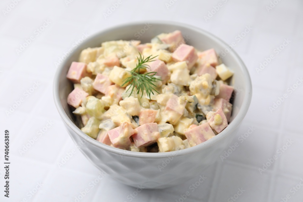 Tasty Olivier salad with boiled sausage in bowl on white tiled table, closeup Tasty Olivier salad with boiled sausage in bowl on white tiled table, closeup