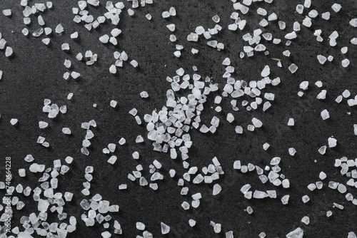 Scattered white natural salt on black table, top view