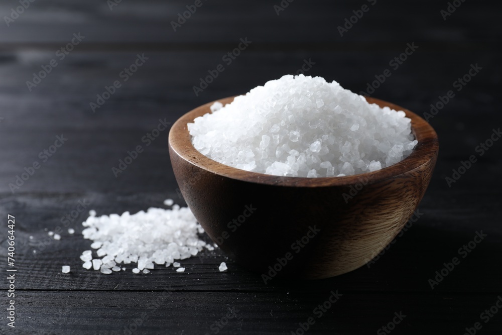 Organic salt in bowl on black wooden table, closeup Organic salt in bowl on black wooden table, closeup