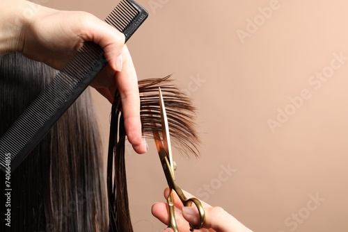 Hairdresser cutting client's hair with scissors on light brown background, closeup. Space for text
