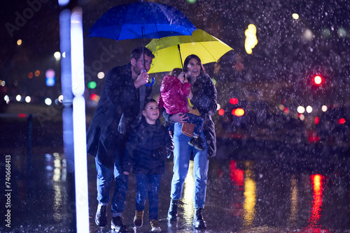In the midst of a rainy urban night, a happy couple takes their children on a stroll through the city streets, heading towards the cinema for a delightful family movie outing