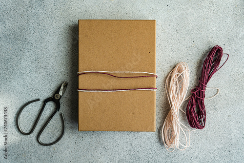 A simple yet elegant gift wrapped in brown paper with a pink and white twine, alongside scissors and additional twine on a textured grey background photo
