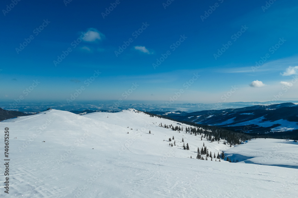 Snow covered meadow with panoramic view of hills and mountains seen from Kor Alps, Lavanttal Alps, Carinthia Styria, Austria. Winter wonderland in Austrian Alps. Ski touring on untouched landscape