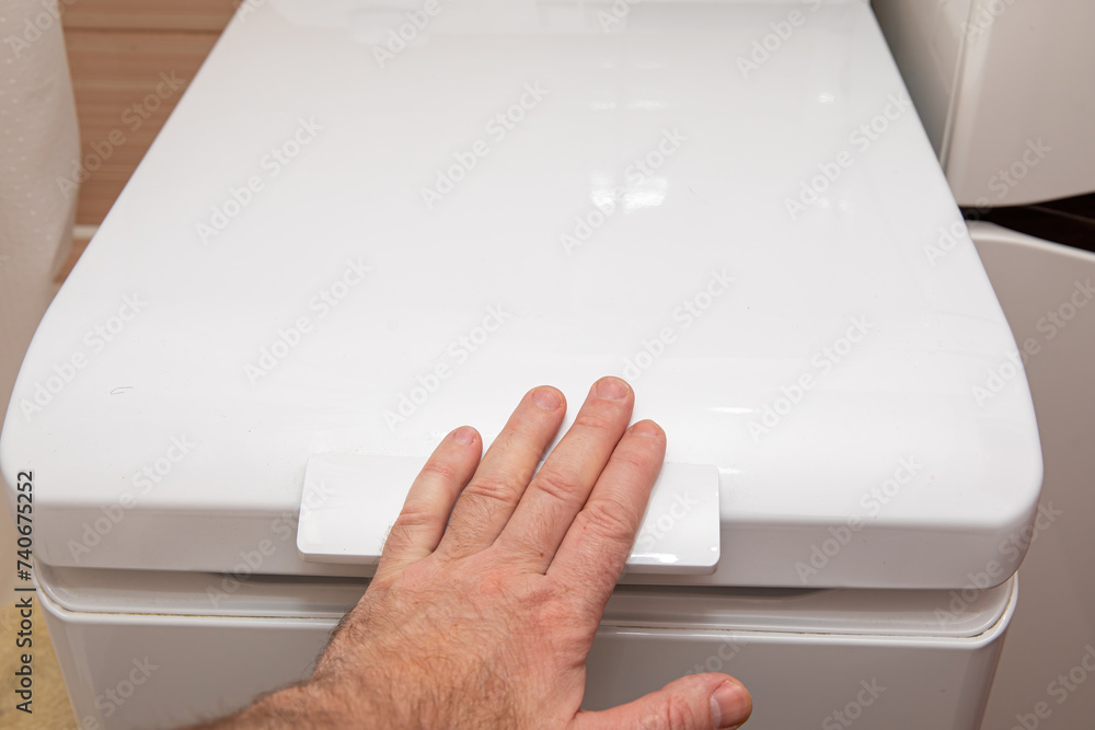 The man closes the lid of the washing machine for washing. The man closes the lid of the washing machine for washing.