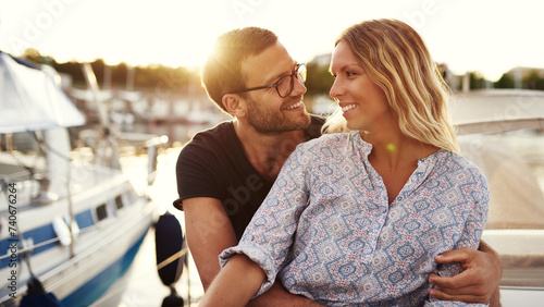 A smiling man looks in love at his girlfriend as they sit on a boat and enjoy the sunset photo