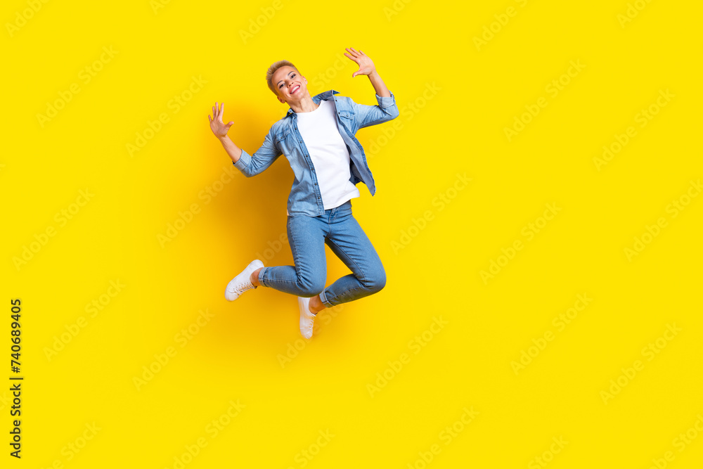 Full length photo of lovely young lady jumping raise hands excited dressed stylish denim garment isolated on yellow color background