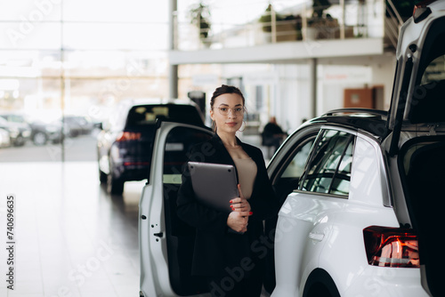 Smiling saleswoman typing on her laptop at new car showroom © Roman