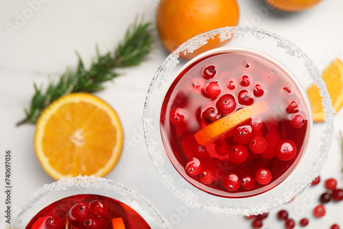 Tasty cranberry cocktail with rosemary and oranges in glasses on white table, flat lay