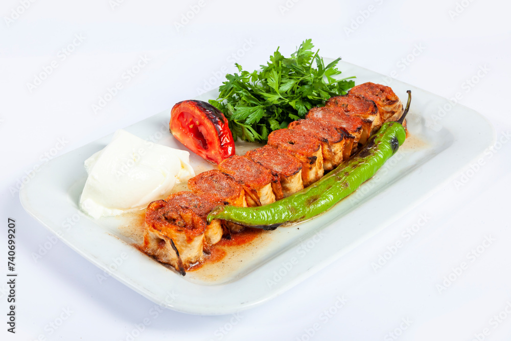 Close up view of traditional grilled beyti kebab rolls with pita bread, yogurt, pepper, tomato and fresh parsley isolated on white background.