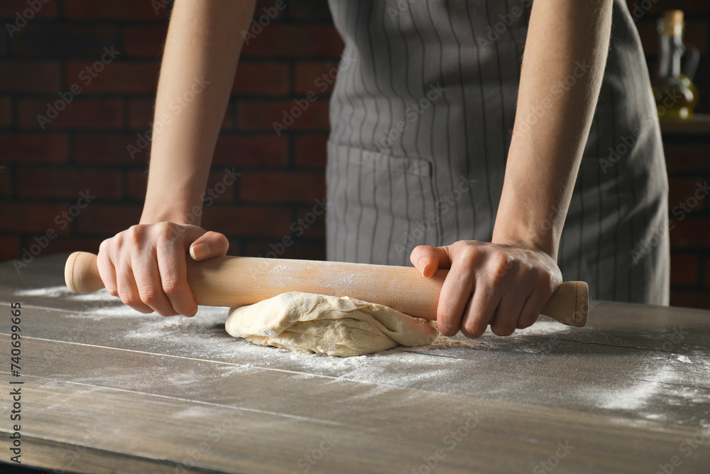 Making bread. Woman rolling dough at wooden table indoors, closeup