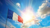 Waving flag of France on bright sunny day high in the blue sky with clouds and sun background as a symbol of freedom and independence day or Bastille Day on July 14