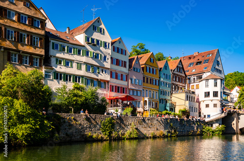 Fototapeta Naklejka Na Ścianę i Meble -  Neckarfront panorama in Tuebingen in Baden-Wuerttemberg Germany on a sunny summer day with colorful renovated facades. People relaxing and chilling on a popular old brick wall above river Neckar.