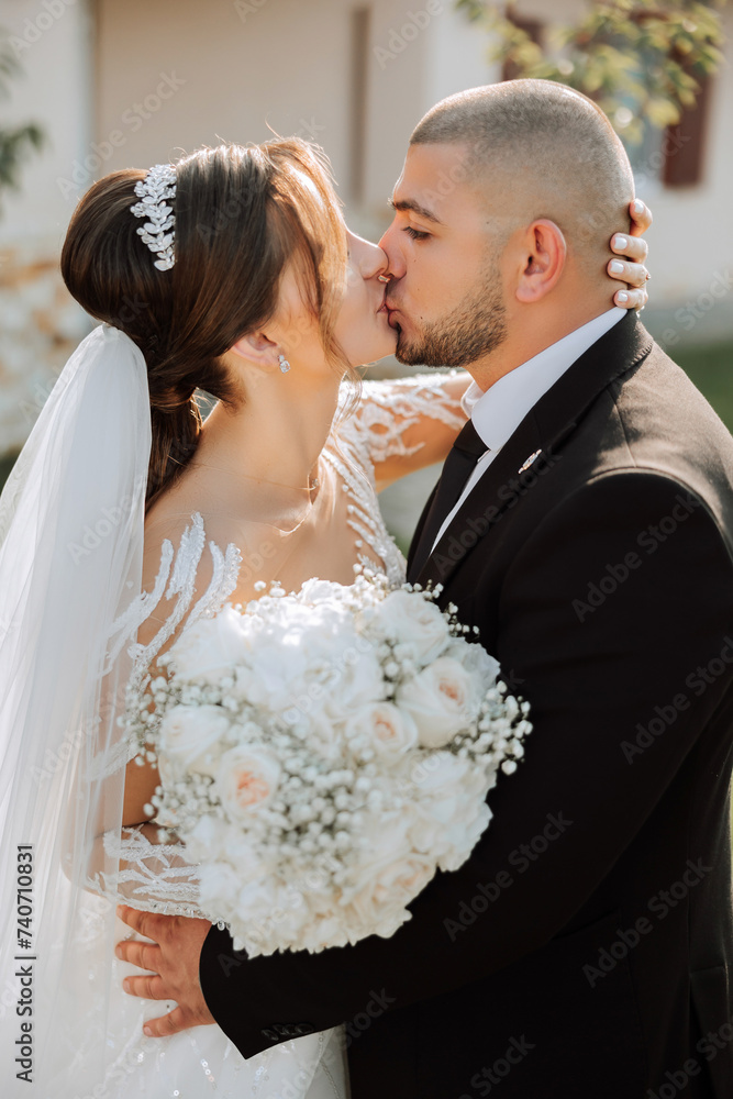 A young bride and groom tenderly embrace in the rays of the autumn sun. Tender and beautiful young girl bride. A man kisses his beloved. Against the background of a beautiful garden