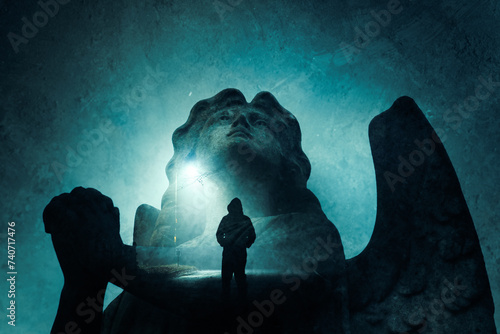 A double exposure of a graveyard angel statue praying. With a spooky hooded figure.  Standing on a street at night. With a grunge edit photo