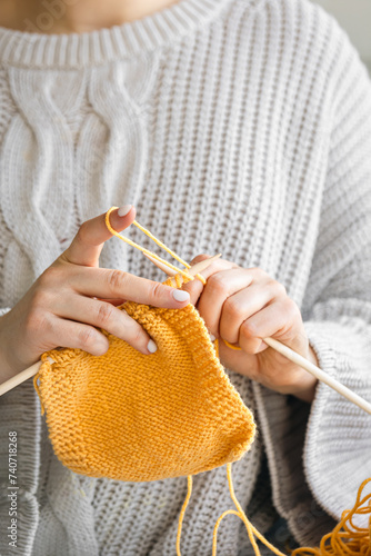 Close-up of female hands knitting yellow wool sweater.