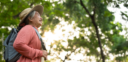 Portrait of Asian mature woman in a hat with backpack behind her back, an Asia active senior woman enjoying nature in autumn park. Standing on a trail in a forest outdoors. Enjoying active travel trip photo
