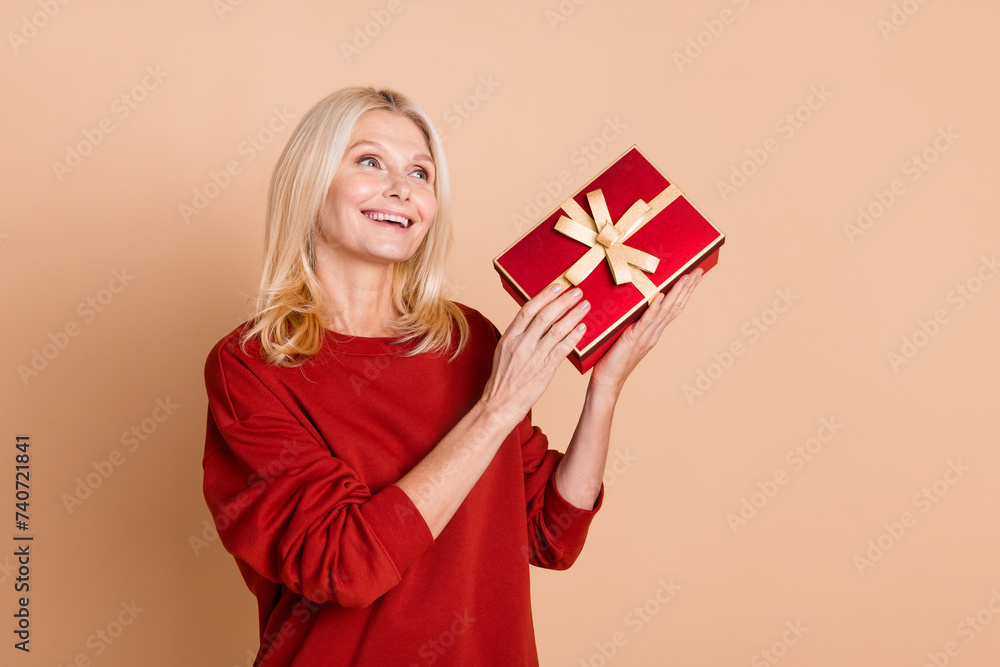 Photo of funky thoughtful woman wear red sweater holding gift box looking empty space isolated beige color background Photo of funky thoughtful woman wear red sweater holding gift box looking empty space isolated beige color background