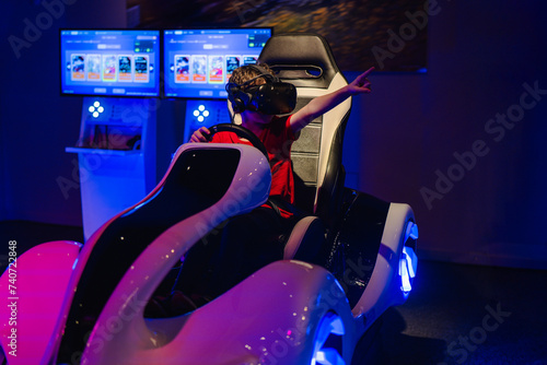 Excited child with a VR headset on gesturing while sitting in a sleek simulator ride at an arcade photo