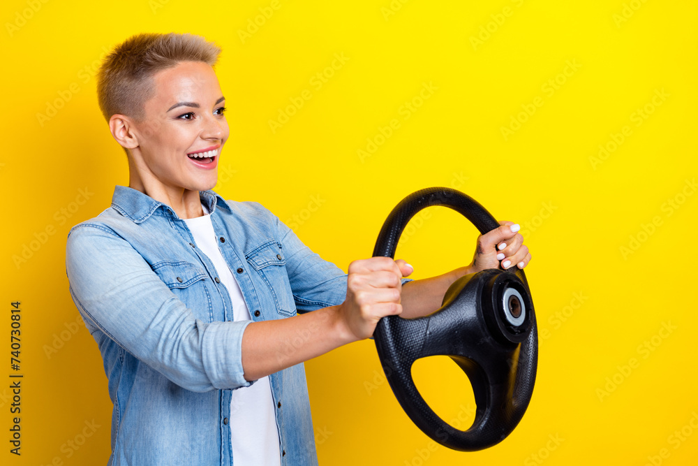 Photo portrait of lovely young lady hold steering wheel look empty space dressed stylish denim garment isolated on yellow color background Photo portrait of lovely young lady hold steering wheel look empty space dressed stylish denim garment isolated on yellow color background
