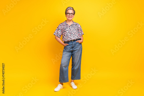Full size photo of pretty retired female posing hands jeans pockets wear trendy leopard print outfit isolated on yellow color background