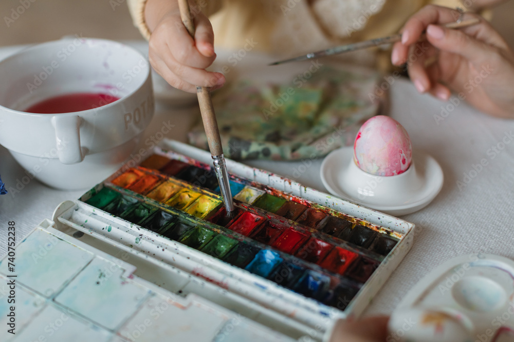 Close-up of a little girl painting eggs for Easter at a table in a cozy kitchen. Easter family traditions. Close-up of a little girl painting eggs for Easter at a table in a cozy kitchen. Easter family traditions.