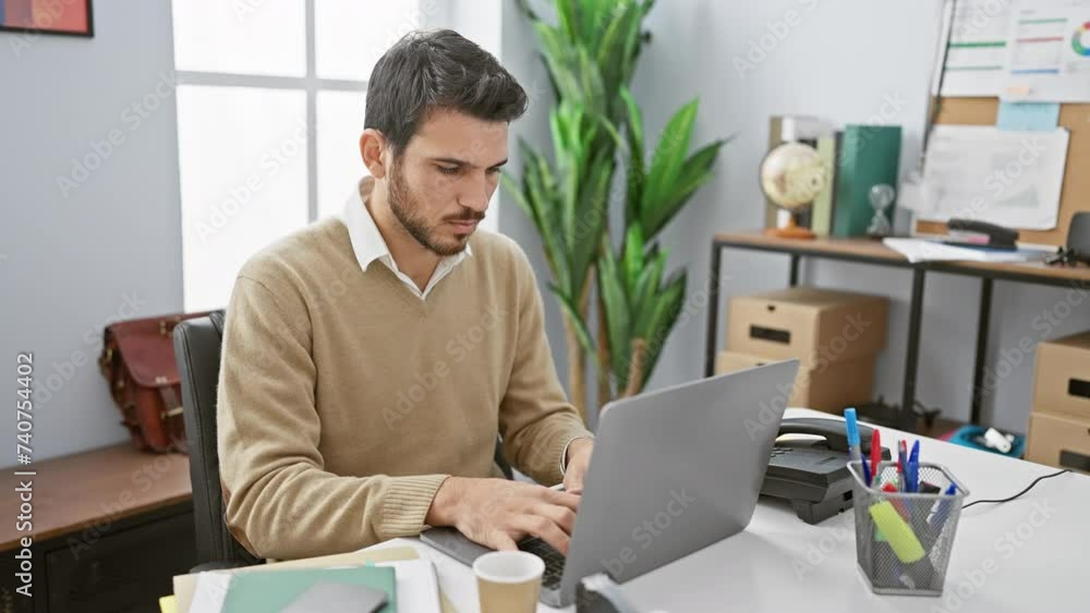 A focused hispanic man with a beard works on a laptop in a modern office, sipping coffee and contemplating. A focused hispanic man with a beard works on a laptop in a modern office, sipping coffee and contemplating.