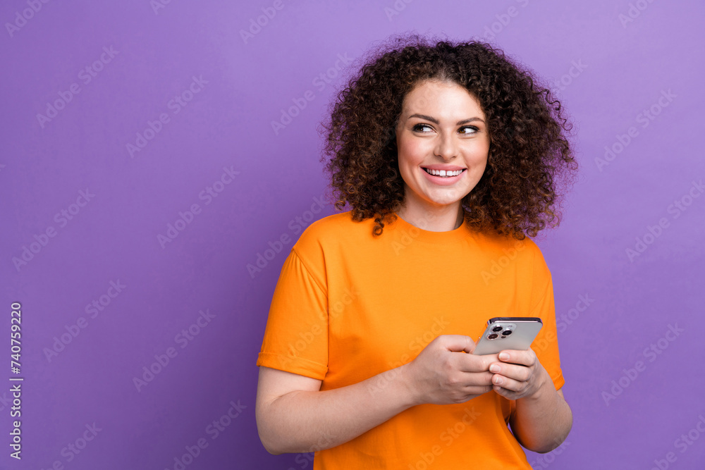 Photo of thoughtful pretty lady dressed orange t-shirt texting modern device looking empty space isolated violet color background Photo of thoughtful pretty lady dressed orange t-shirt texting modern device looking empty space isolated violet color background