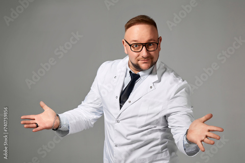 Portrait of friendly male doctor in uniform talking and gesturing at camera, posing on gray background with open hands and smiling, copy space © andrey_orlov