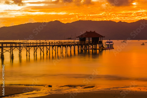 A wooden pier stretches out into a calm bay at sunset  with mountains in the background.