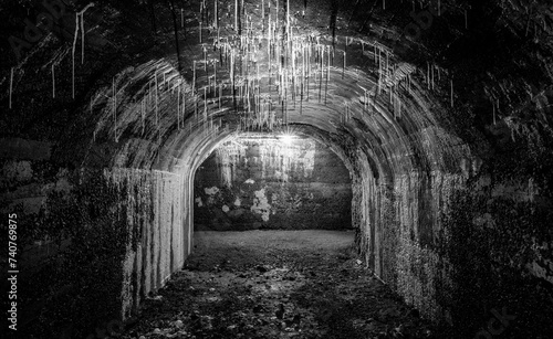 Historic bunker tunnel from world war 2 built with reinforced concrete now is a scary lost place in the dark with stalactites, old light bulbs, wet walls, spooky atmosphere. Black and white vintage.