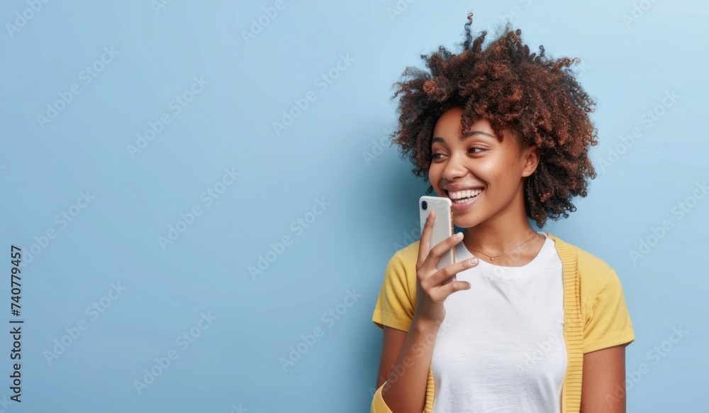 Half length shot of Afro woman holds mobile phone, enjoys nice talk online in social networks, reads funny article in internet, uses cellular isolated over blue background. - obrazy, fototapety, plakaty 