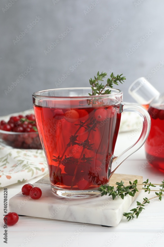 Tasty hot cranberry tea with thyme and fresh berries in glass cup on white wooden table Tasty hot cranberry tea with thyme and fresh berries in glass cup on white wooden table
