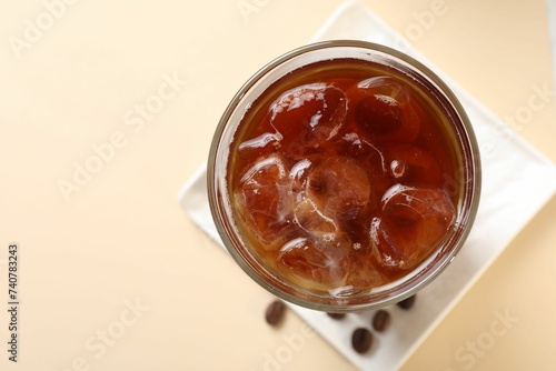 Refreshing iced coffee in glass on beige table, top view. Space for text