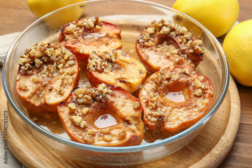 Tasty baked quinces with walnuts and honey in bowl on wooden table, closeup
