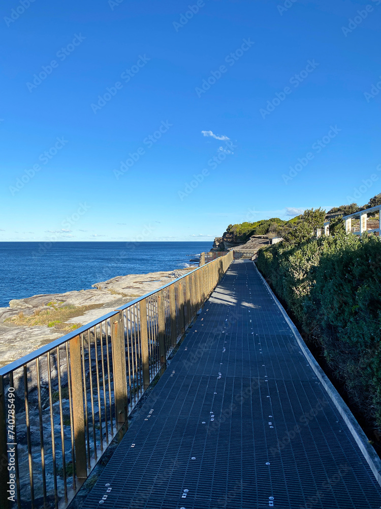 Obraz premium Boardwalk to the beach. Fence and bridge on the sea coast. Walkway near the blue turquoise ocean. Pier in the sea.