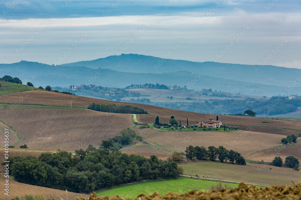 Autumn moody skies landscape in the mountain region of Tuscany, Italy with plowed fields, mist and beautiful cypress trees. Travel tourism destinations