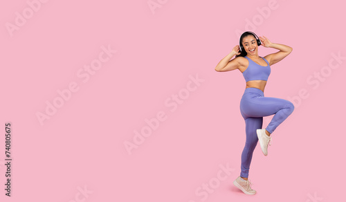 Joyful woman dancing in sportswear with headphones on pink backdrop