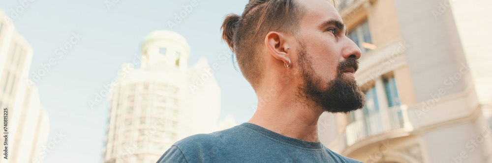 Fototapeta premium Profile of young smiling man with beard walking down the street, Panorama