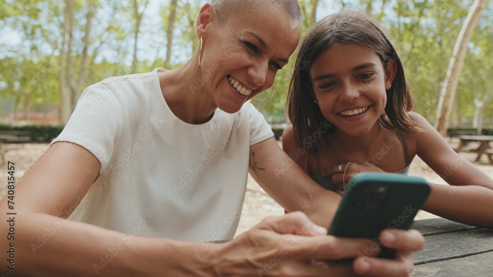 Happy mother and daughter sitting in the park using mobile phone Happy mother and daughter sitting in the park using mobile phone