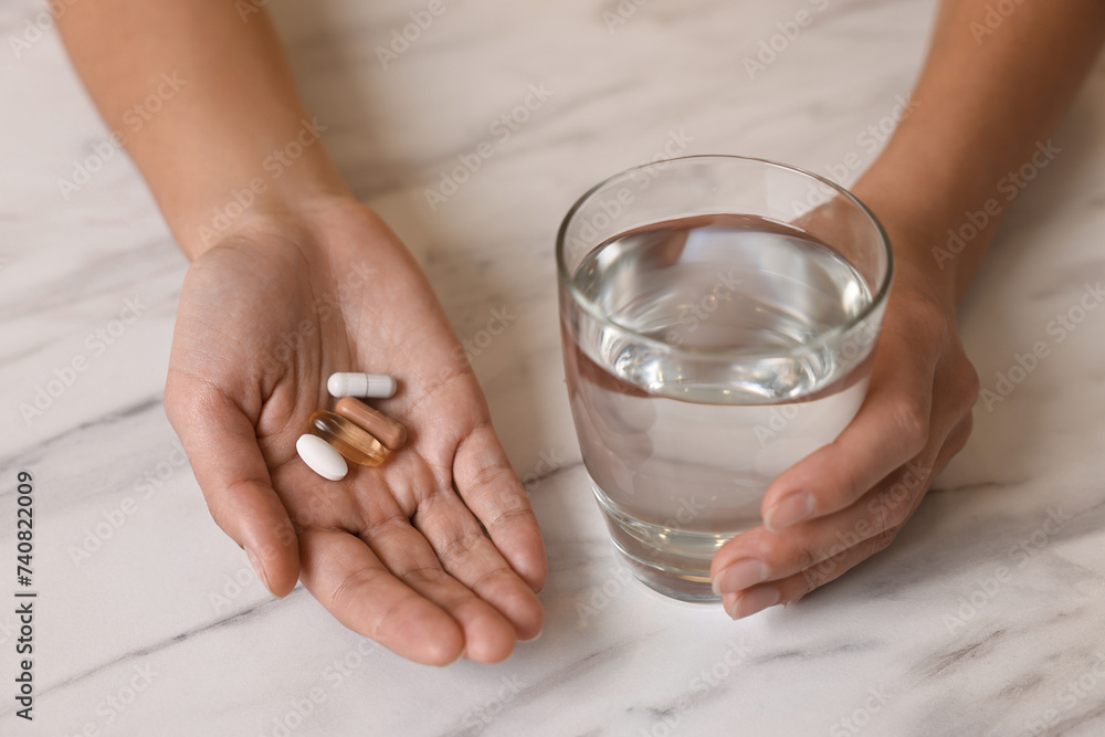Woman with vitamin pills and glass of water at white marble table, closeup Woman with vitamin pills and glass of water at white marble table, closeup